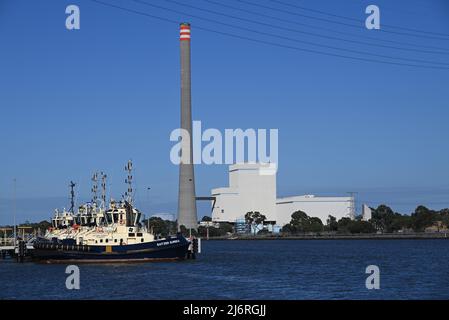 Docked tug boat Svitzer Eureka, alongside other tug boats on the Yarra River, with Newport Power Station in the background across the river Stock Photo