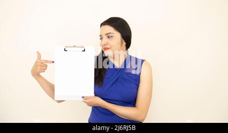 Beautiful and successful CEO assistant, wearing blue blouse, satisfied, pointing with his hand information on a clipboard, on white background. Stock Photo