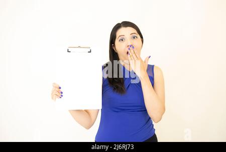 Beautiful and successful CEO assistant, wearing blue blouse surprised showing results, holding a clipboard with her hand, on white background Stock Photo