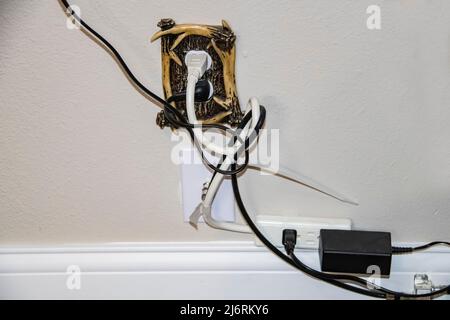 Messy electric cords - too many plugged into one decorative electrical outlet plus cable - all in a tangle Stock Photo