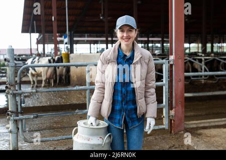 Milkmaid with aluminium cans near open cowshed at dairy farm Stock Photo