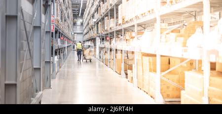 The Back view of Asian man pushing the cart trolley that carried boxes to arrange and put on the shelf in the warehouse. Stock Photo