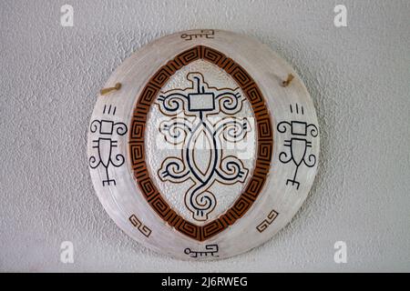 Wall decor, white plate crafts with brown details and black amazon designs on a white textured wall Stock Photo