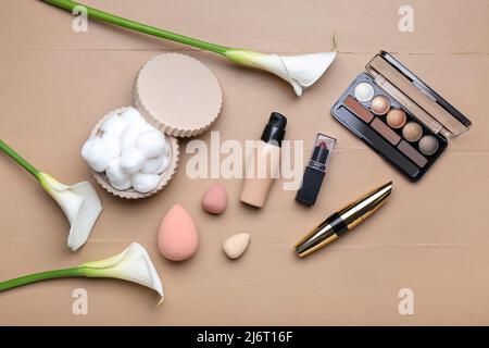 Composition with decorative cosmetics, makeup sponges, cotton balls and calla lilies on color wooden background Stock Photo
