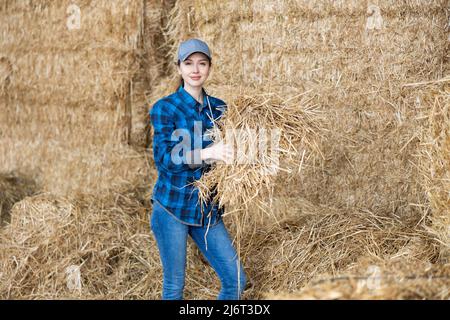 Young female farmer standing in hayloft with hay in hands