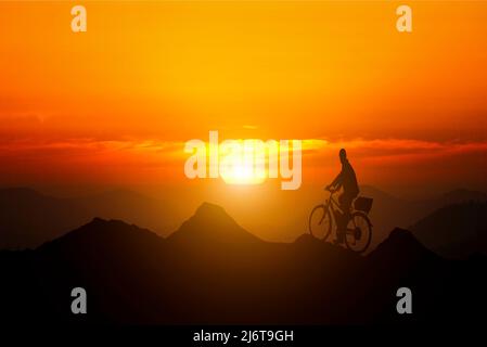 Leadership and goals. A man standing on top of a mountain on a bicycle watching the sunset. Conceptual image composite. Stock Photo