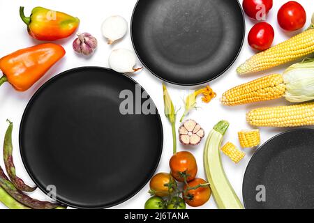 Creative layout made of autumn vegetables. Tomatoes, onion, carrot, garlic, red beet, pepper, zucchini, corn, green haricot and black plate on white s Stock Photo