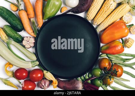 Pattern made of autumn vegetables. Tomatoes, onion, cucumber, carrot, garlic, red beet, pepper, zucchini, corn, green haricot and black plate on white Stock Photo