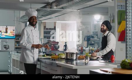 POV of multiethnic team of chefs recording cooking show video, having fun and preparing ingredients for gourmet dish. Authentic cooks making meal preparations for online class program. Stock Photo