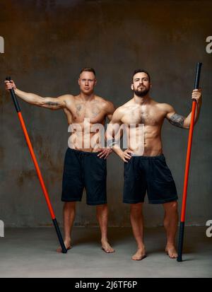 People stand together and practice sticks. Karate masters posing with sticks in the studio together. Stock Photo