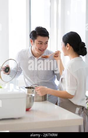 In the family kitchen, husband lifted the lid of the soup pot and the wife scooped up a spoonful for him to taste - stock photo Stock Photo