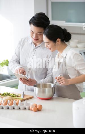 In the family kitchen, a young couple enjoy cooking together and using tablets to check future purchases - stock photo Stock Photo