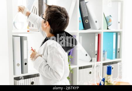 School boy looking at transparent liquid in bottle during chemistry experiment in elementary science class. Clever pupil in lab during test back view Stock Photo