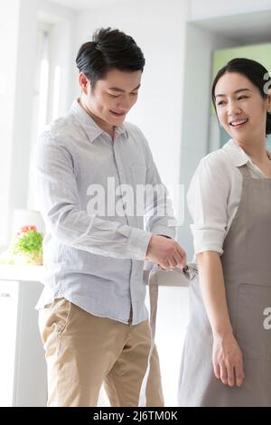 In the family kitchen, husband helped his wife put on the apron, and she looked back in relief - stock photo Stock Photo