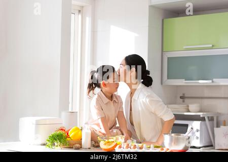 Family kitchen parentage. Young mother in the kitchen with her child and kissing her daughter's forehead. - stock photo Stock Photo