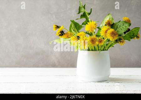 Mock up creation. White wooden table with grey concrete background, dandelions in vase and copy space on the left Stock Photo