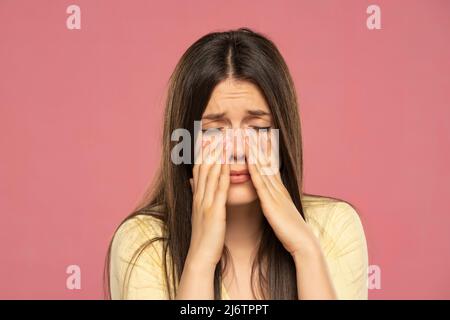 Sinus pain, sinus pressure, sinusitis. Sad woman holding her nose because sinus pain on a pink background Stock Photo