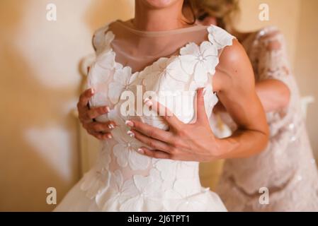 Gorgeous, blonde bride in white luxury dress is getting ready for wedding. Morning preparations. Woman putting on dress Stock Photo