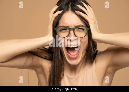 Closeup portrait stressed frustrated woman with eyeglasses screaming isolated on beige background. Negative human emotion facial expression reaction a Stock Photo