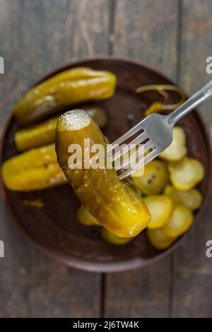 Salted pickled cucumbers on a fork in the foreground. in the background a plate of cucumbers Stock Photo