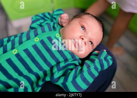 Newborn baby in striped clothes lies with arms raised up Stock Photo