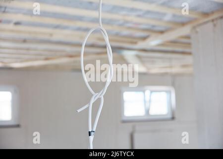 Gray power cable with knots hangs from ceiling in room at new build house Stock Photo