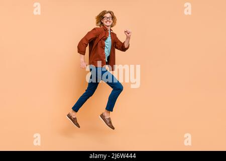 Full length body size view of attractive cheerful motivated guy jumping running isolated over beige pastel color background Stock Photo