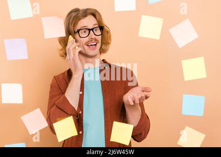 Portrait of handsome trendy cheerful red-haired guy memo card wall talking on phone isolated over beige pastel color background Stock Photo