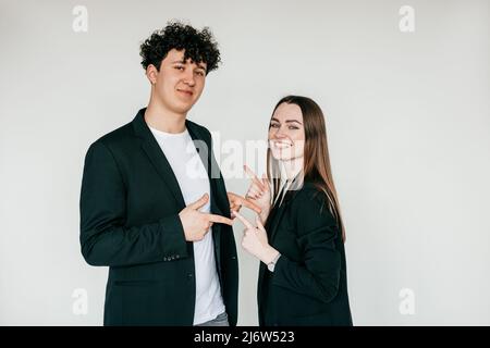 Portrait of young couple wearing black clothes. Young happy man standing near smiling woman, pointing at each other. Stock Photo