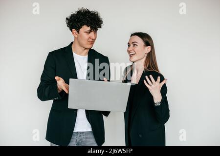 Portrait of young overemotive couple wearing black. Young pleased man holding ans showing laptop to overjoyed woman. Stock Photo