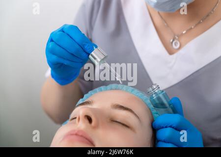 Hands of cosmetologist dripping nourishing oil facial skin of young woman in spa salon. Facial treatment and skincare concept. Stock Photo