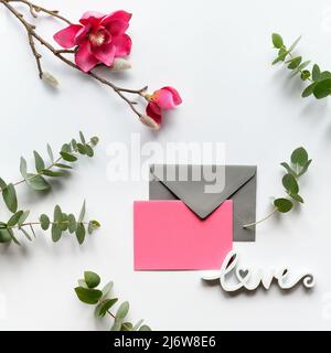 Pink magnolia flowers on twigs, fresh eucalyptus leaves. Blank pink card with grey envelope. Stock Photo