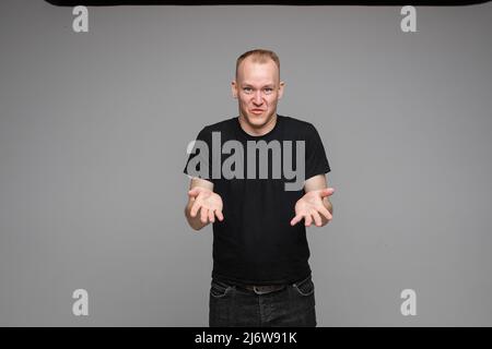 picture of handsome caucasian male explain something keeping hands in front of him isolated on grey background Stock Photo