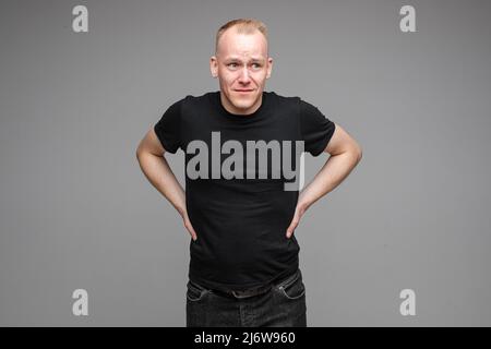 handsome caucasian man with short fair hair keeping hands on the belt and thinks about something sad Stock Photo