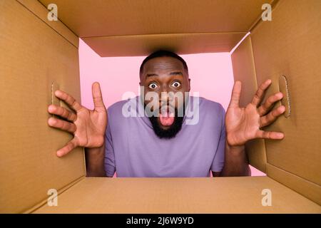 Low angel bottom view photo of funky shocked guy dressed violet t-shirt looking inside paper box isolated pink color background Stock Photo