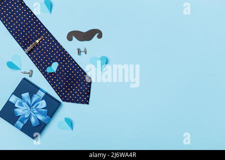 Father's day concept postcard. Men's tie box with a gift paper mustache cufflinks on a blue background. Stock Photo