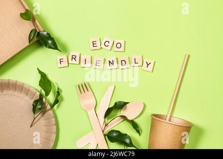 Disposable cup, plate and wooden cutlery on a green background Stock Photo