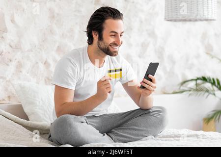 Positive young man shopping on internet, using phone Stock Photo