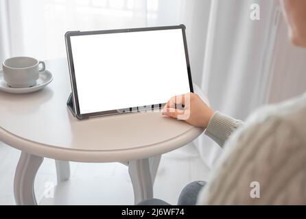 mockup tablet on white table. Unrecognizable woman using digital tablet with blank screen, sitting by table with coffee, mockup for mobile app or webs Stock Photo