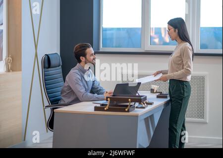 Assistant handing papers to her boss in his office Stock Photo