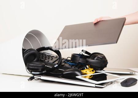 Woman hand put used laptop to recycling bin full of old computers, phones, tablets, cords and electronic devices. Planned obsolescence, e-waste Stock Photo