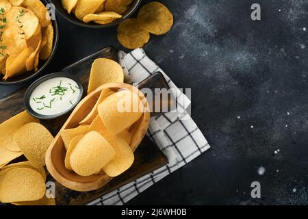 Unhealthy food. Snacks. All classic potato snacks with peanuts, popcorn and onion rings and salted pretzels in bowl plates on black concrete backgroun Stock Photo