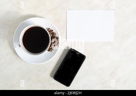 A cup of coffee with coffee beans, mobile phone and empty blank on the table Stock Photo