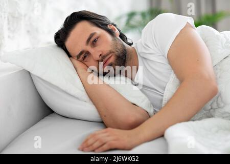 Depressed man laying in bed alone, looking at copy space Stock Photo