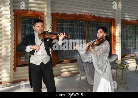 Duo of violinists. A man in a tailcoat and a woman in an evening dress play the violin Stock Photo