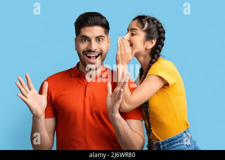 Cheerful Arab Woman Sharing Secrets With Excited Boyfriend, Whispering To His Ear Stock Photo