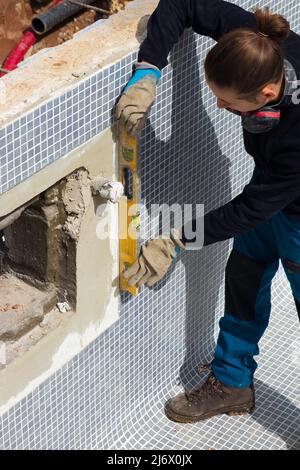 Young worker using bubble level for walls full of tiles in a swimming pool area under construction Stock Photo