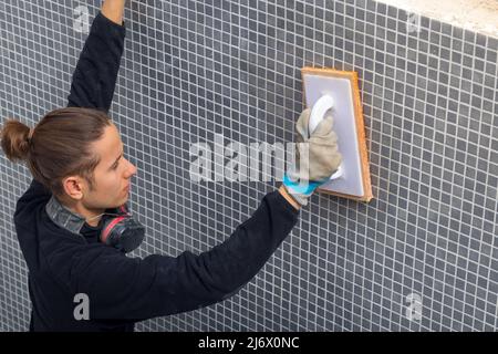 Young laborer man working on a swmming pool construction tiling with a plastering sponge trowel Stock Photo