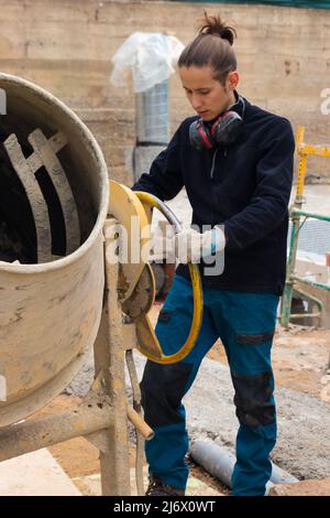 Construction man worker making and preparing concrete in the cement mixer at construction site Stock Photo