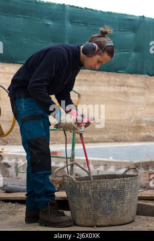 Young working man using drill mixing machine construction products with anti-sound headphones on in a construction site Stock Photo